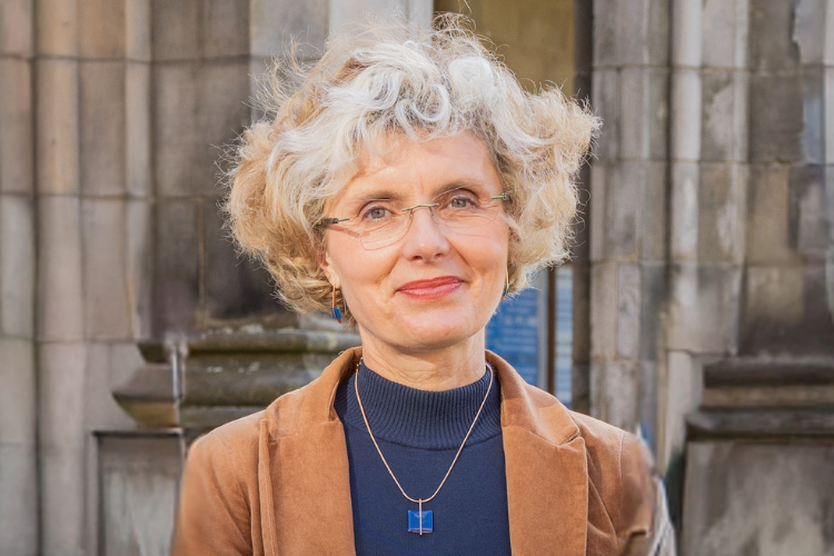 a woman smiles at the camera, standing in a university quad