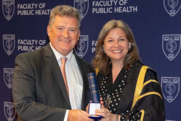 A man accepts an award from a woman in a gown, both smiling